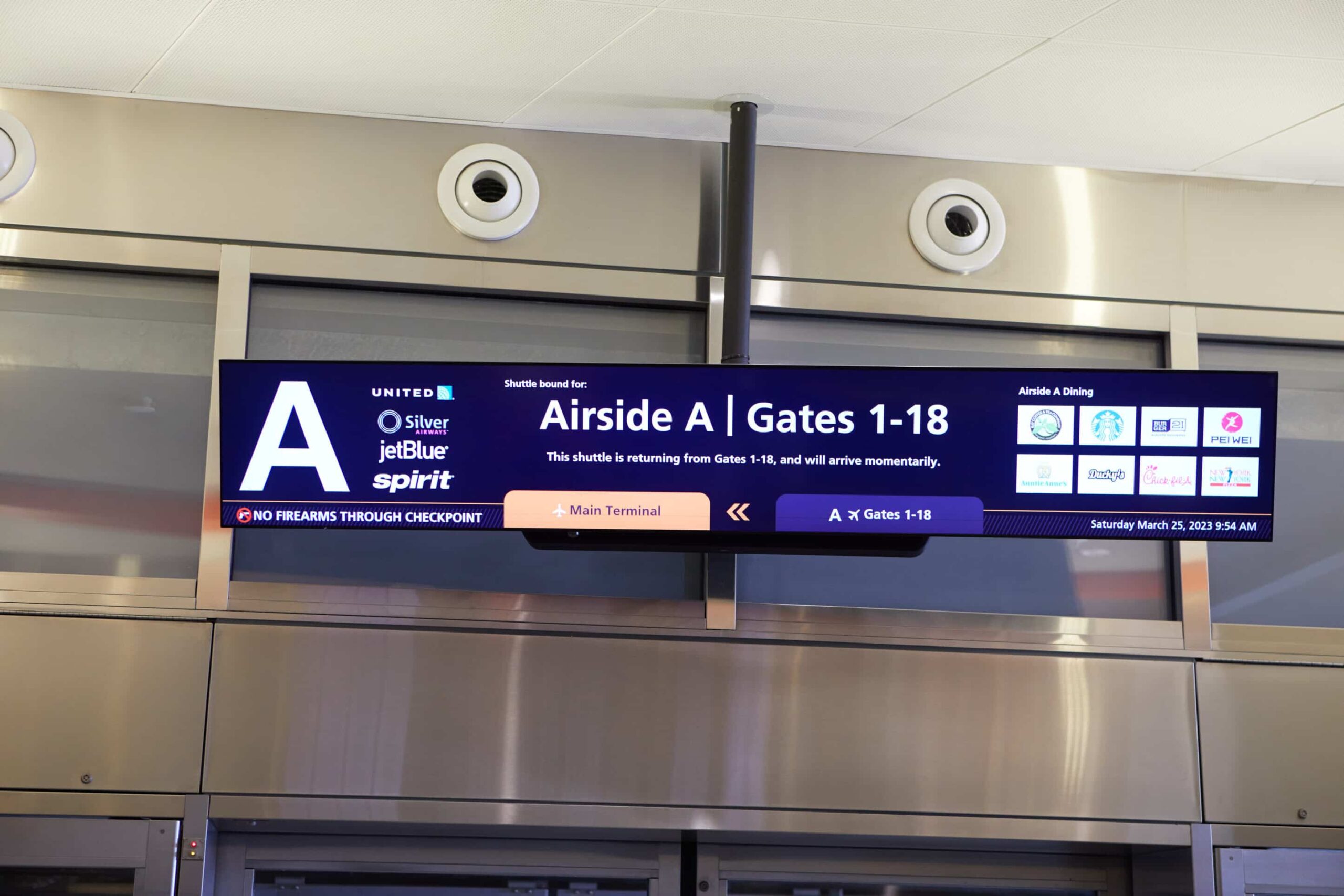 Airport sign: Airside A, Gates 1-18 (United, Silver, JetBlue, Spirit). Shuttle: Gates 5-18. No firearms. March 25, 2023.