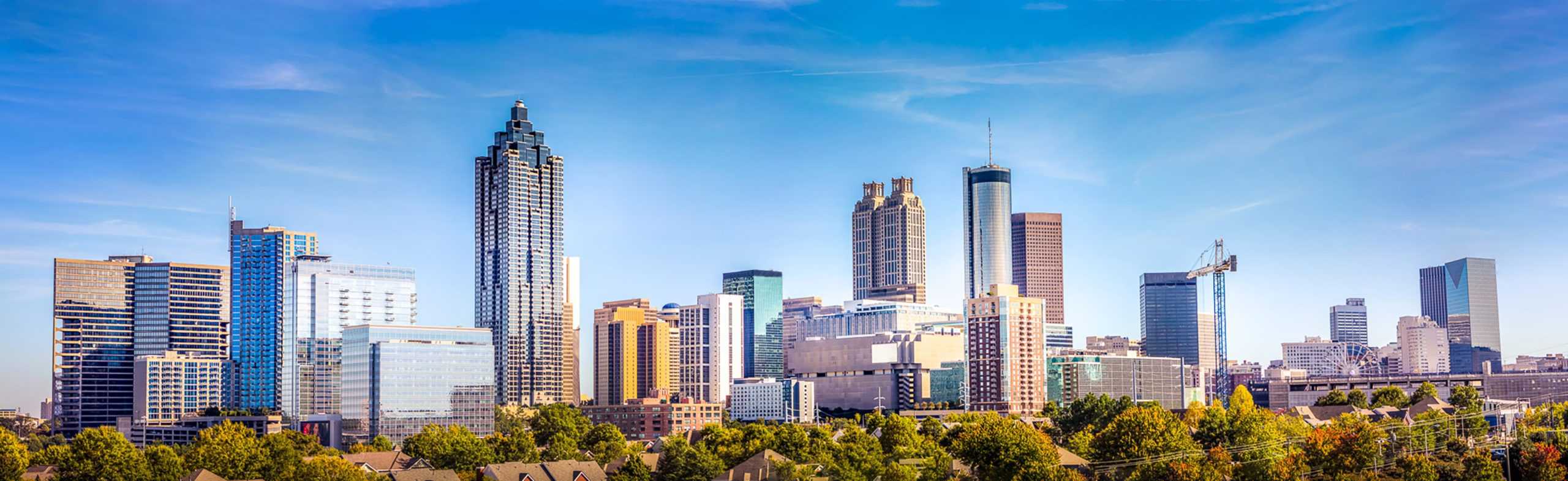 City skyline with skyscrapers, trees, low-rises; clear sky, crane hints at growth.