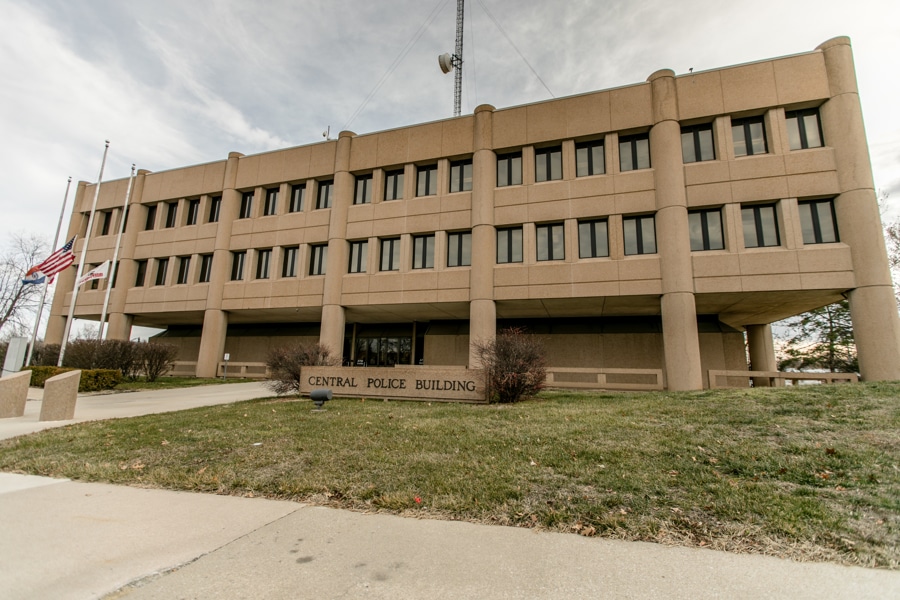 Central Police Building: a large beige structure with flags, grassy forefront, multi-story facade, and a cloudy sky.
