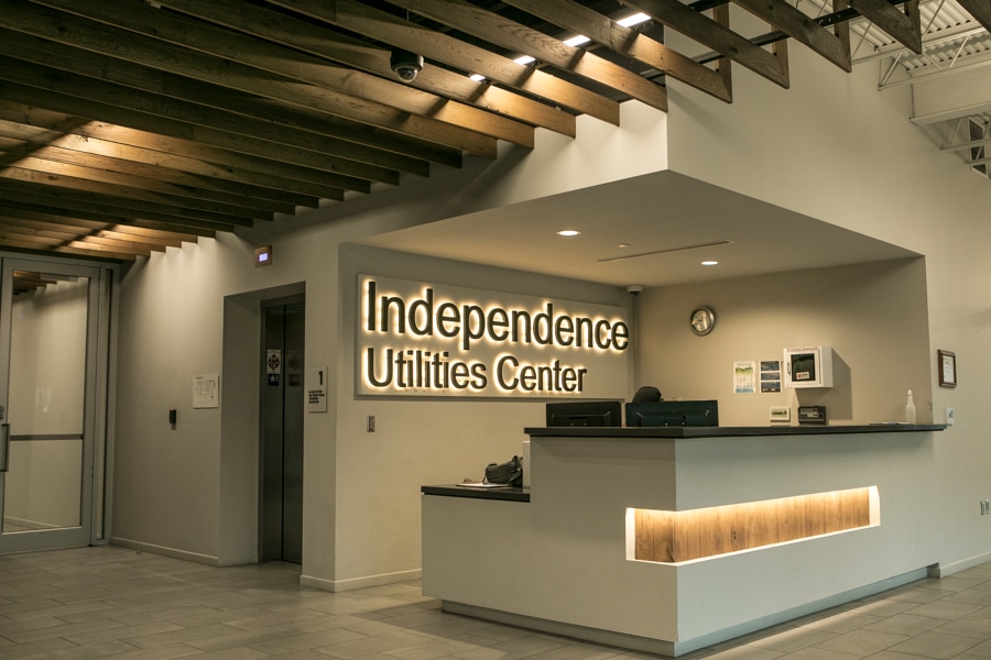 Maintain the Independence Utilities Center lobbys modern design: wooden ceiling, lit sign, tiled floor, and backlit reception desk.